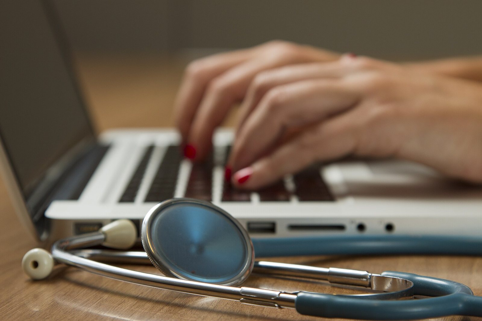 Hands typing on a laptop with a stethoscope beside it