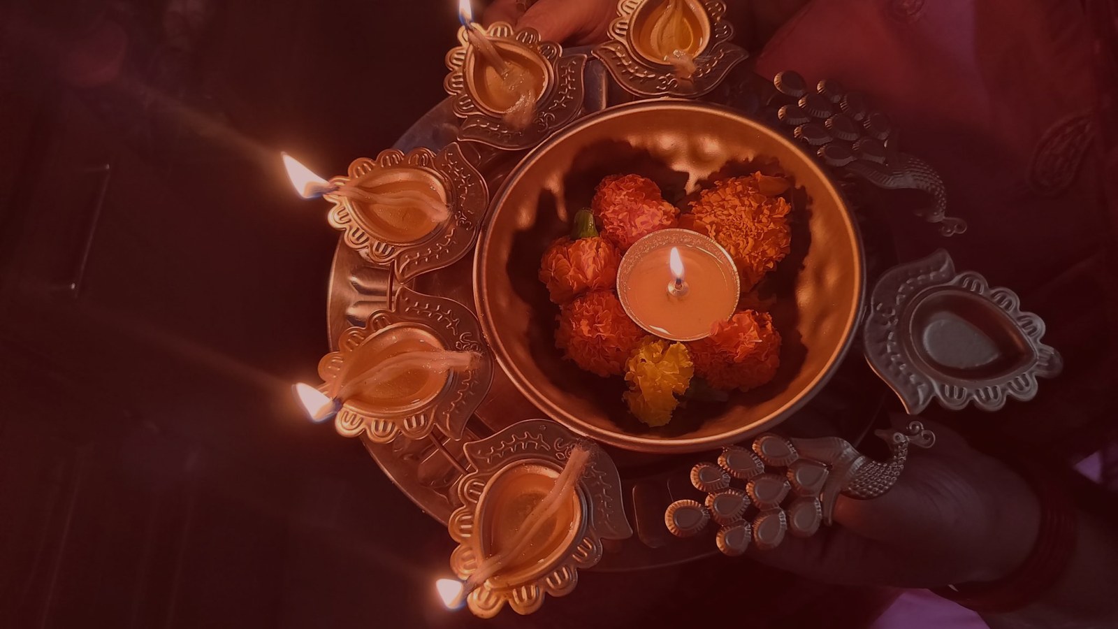 A ring of lit oil lamps around a bowl of marigolds